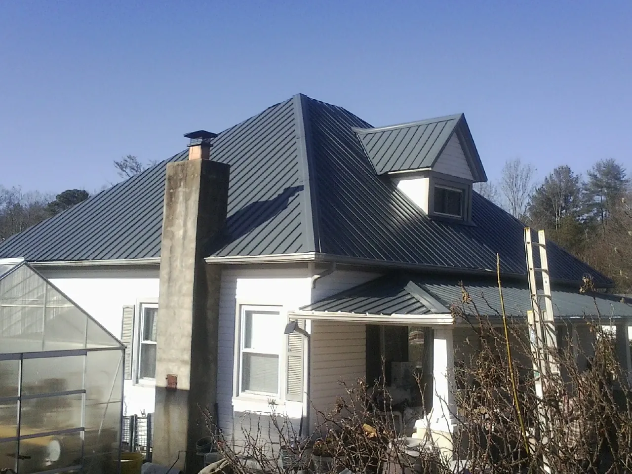 Dark blue standing seam metal roof on a white farmhouse with dormer — Slate & Tile Roof Repair by Roofing Brothers in Coopersville