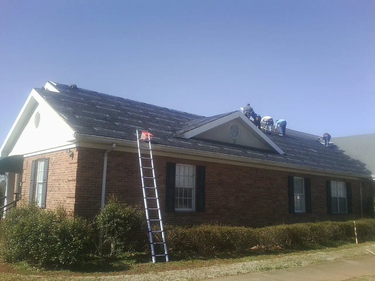 Crew tearing shingles off a brick ranch roof with a ladder set — Emergency Roof Repair work by our crew in Coopersville