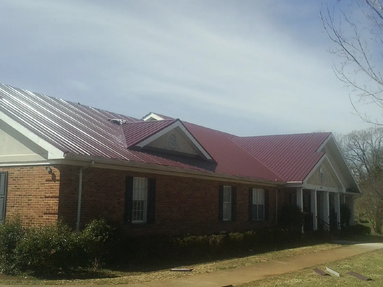 Red metal roof with gabled entries on a long brick building, from a Hail Damage Roof Repair job in Coopersville