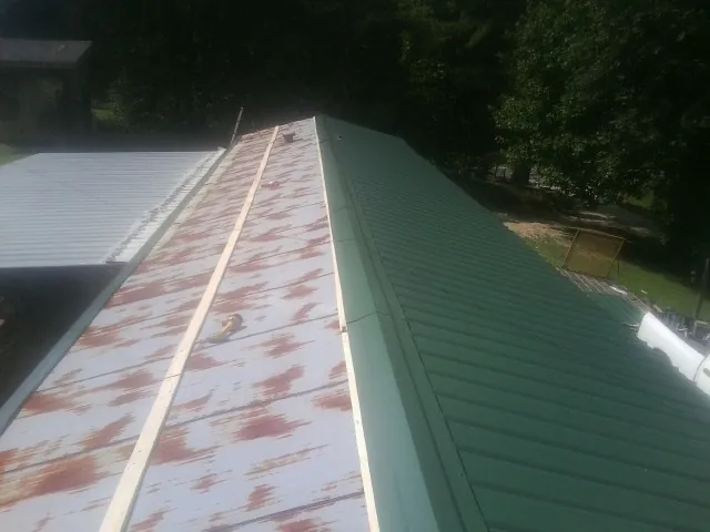 Old rusted panels beside newly installed green metal roofing — Wind Damage Roof Repair by Roofing Brothers in Coopersville