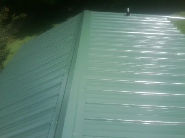 New green metal panels meeting at the ridge of a roof — Flat Roof Repair work by our crew in Coopersville