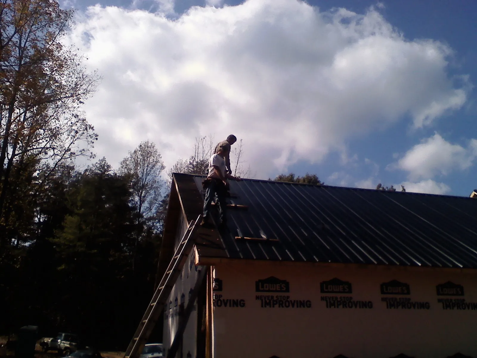 Roofer fastening dark metal panels high against a cloudy sky, from a Roof Inspection job in Coopersville