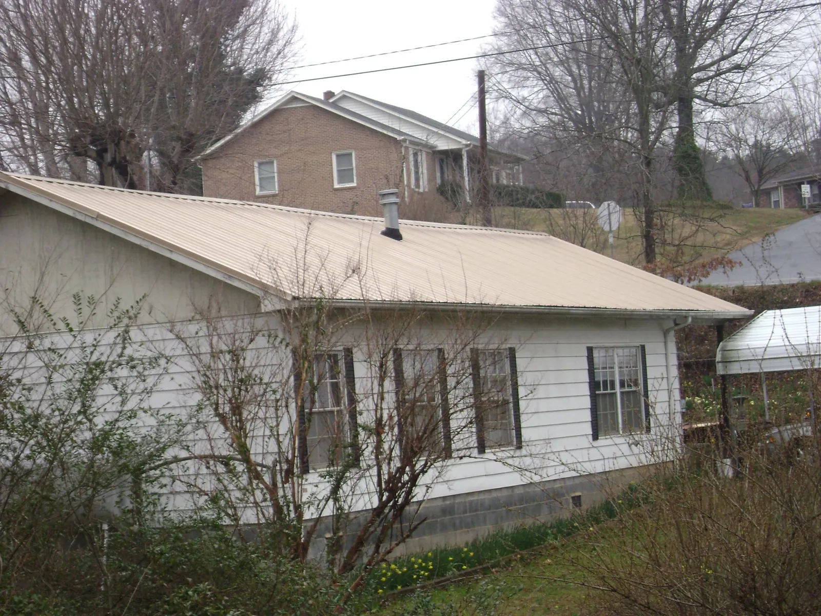 Tan metal roof on a white sided house set into a hillside — Commercial Roofing by Roofing Brothers in Coopersville