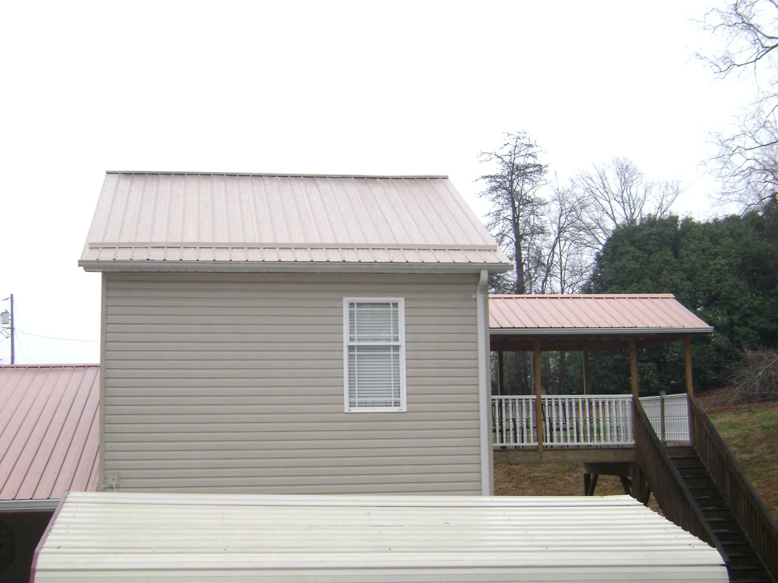 Tan metal roofs on a two story addition and attached porch, from a Roof Replacement job in Coopersville