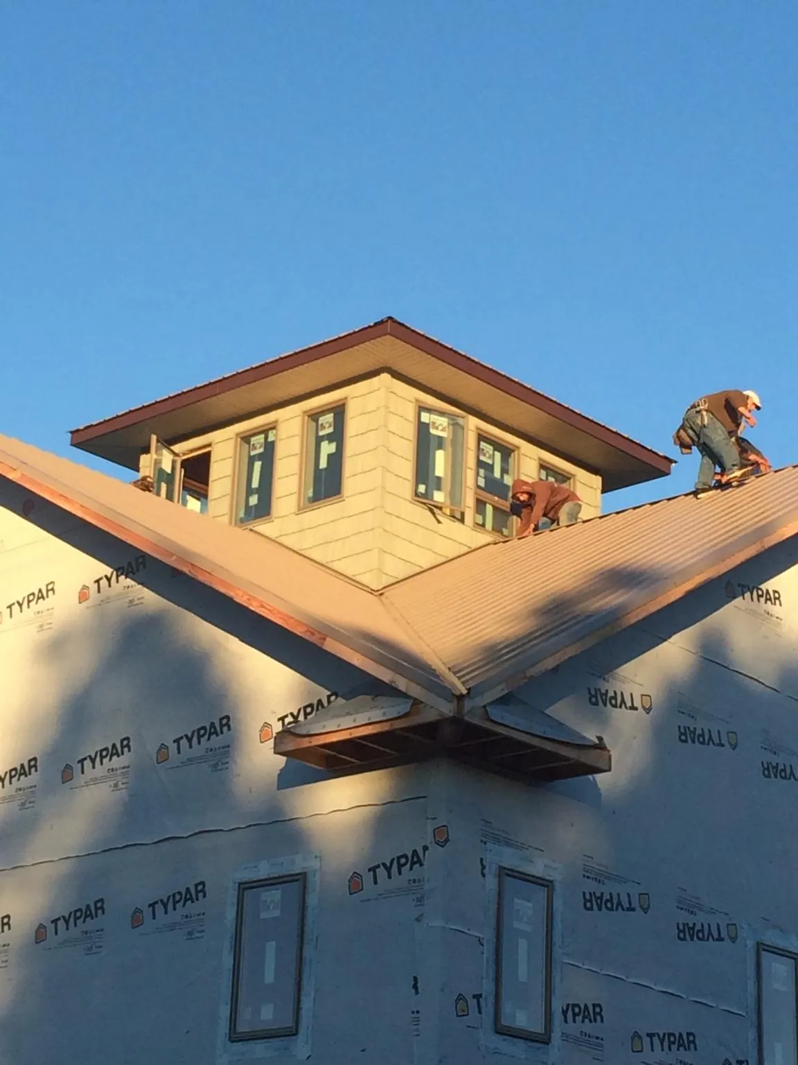 Roofers working around a rooftop cupola on a new metal roof at sunset — Roof Waterproofing in Coopersville by Roofing Brothers
